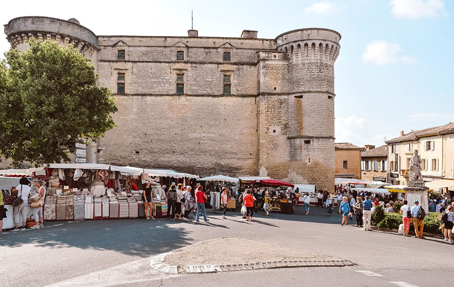 A scene of the Gordes market in the town square with Gordes Castle in the background