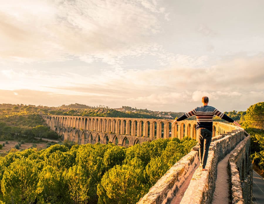 A solo traveller walks across an ancient aqueduct at sunset